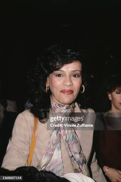 American singer and actress Marilyn McCoo, wearing hoop earrings with a scarf and a beige jacket, April 1982.