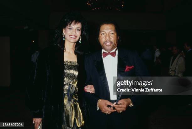 American singer and actress Marilyn McCoo, wearing a gold outfit beneath a black coat, and her husband, America musician Billy Davis Jr, wearing a...