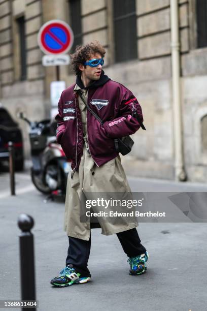 Guest wears a blue electric sunglasses, a black hoodie sweater, a burgundy shiny with red / black / white embroidered yoke bomber coat, a beige long...