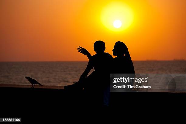 Young Indian couple sit on seawall at sunset at Nariman Point, Mumbai, formerly Bombay, India