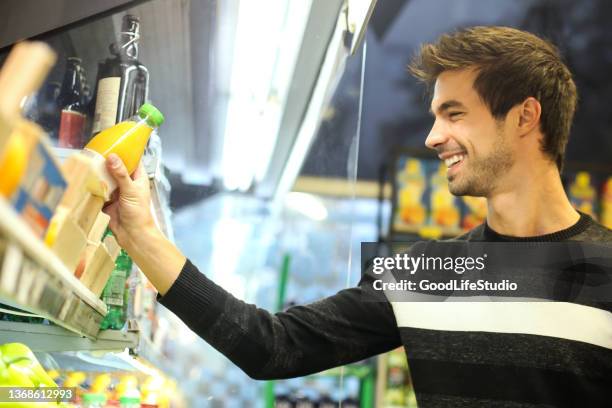 young man buying orange juice - cornershop stockfoto's en -beelden