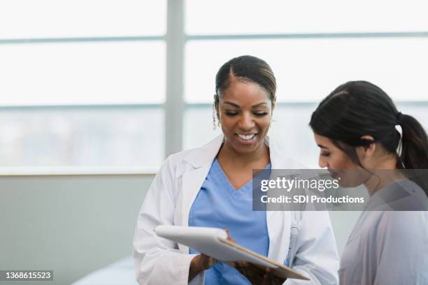 lächelnde ärztin und glückliche patientin lesen krankenakte - woman talking doctor stock-fotos und bilder