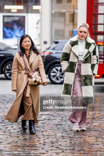 Guest wearing a light brown coat, a brown dress, black boots and a bag witt multibrown colores and a guest wearing a big checked green-beige coat,...