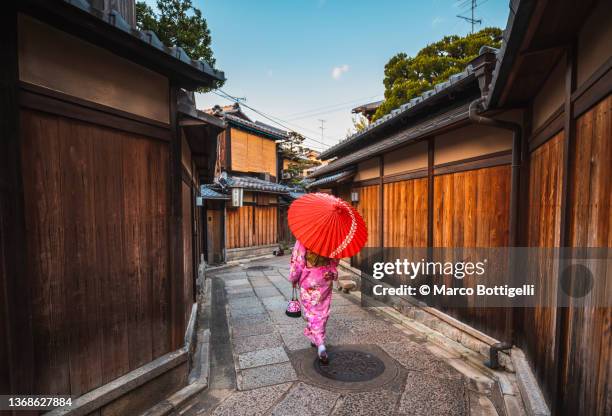 woman dressed in kimono holding red umbrella walking in kyoto's old town - kyoto city stock pictures, royalty-free photos & images