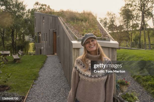 uk, devon, tiverton, portrait of smiling woman standing in front of modern wooden house with grass on roof - green roof stock pictures, royalty-free photos & images