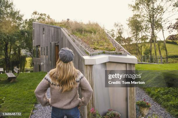 uk, devon, tiverton, rear view of woman standing in front of modern wooden house with grass on roof - dachbegrünung stock-fotos und bilder