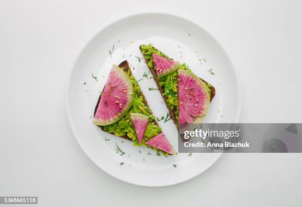 avocado toast: dark bread, mashed avocado, watermelon raddish sandwich over white background. - avocado toast white background stockfoto's en -beelden