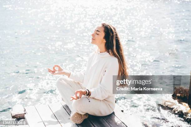 young woman meditating at seashore. - spiritual healing stock pictures, royalty-free photos & images