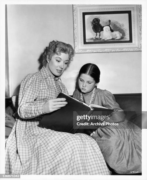 Greer Carson and Donna Corcoran sit reading a book together in a scene from the film 'Scandal At Scourie', 1952.