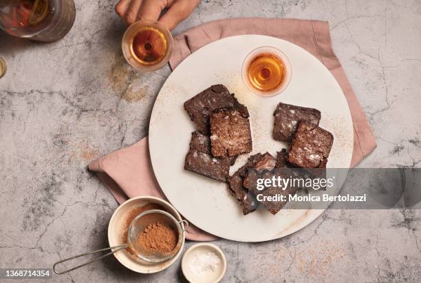 home made brownies on white marble plate with cognac glasses and cocoa sifter - brownie stock pictures, royalty-free photos & images
