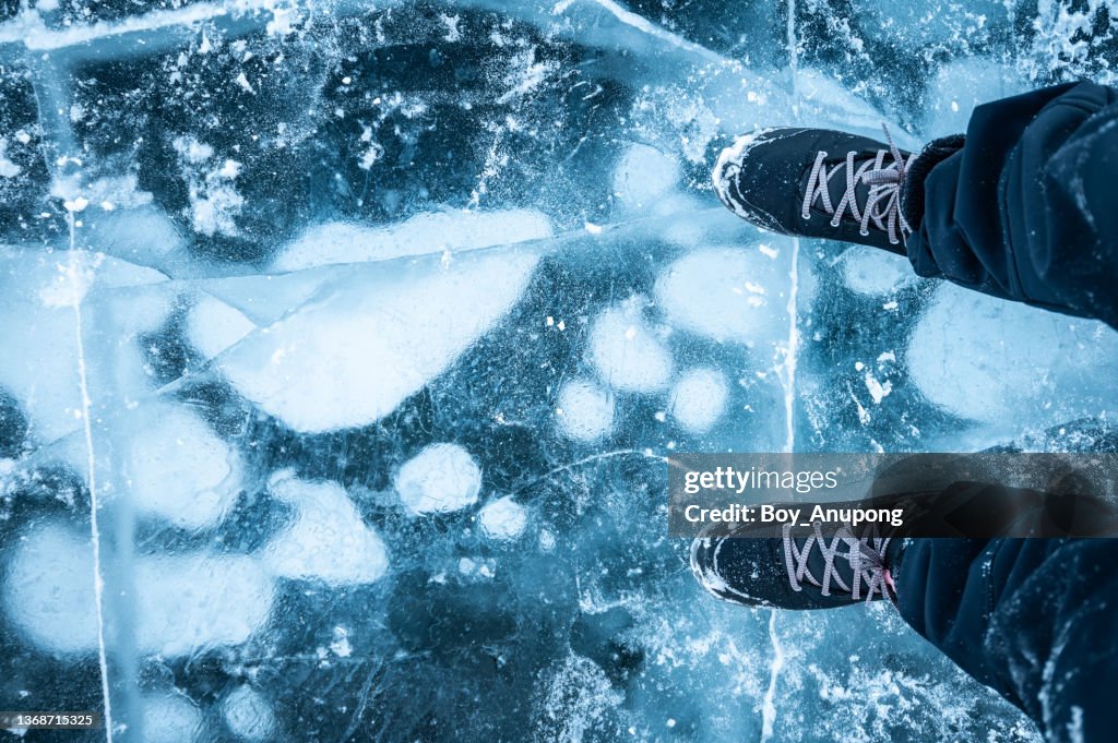 A foot of tourist standing on the cracks surface of Baikal lake with frost methane bubbles in winter season.