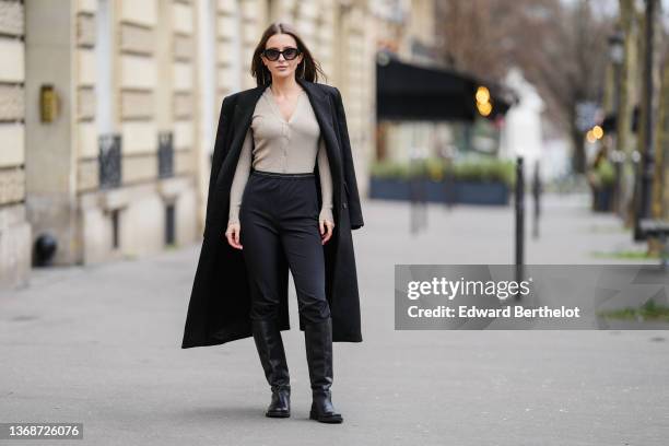 Diane Batoukina wears sunglasses from Prada, a black long winter coat from Zara, a gold beige shiny ribbed V-neck buttoned long sleeves cardigan from...