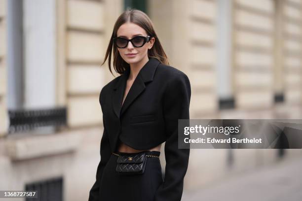 Diane Batoukina wears black sunglasses from YSL / Saint Laurent Paris, a black oversized cropped blazer jacket from Choux, a black shiny leather...