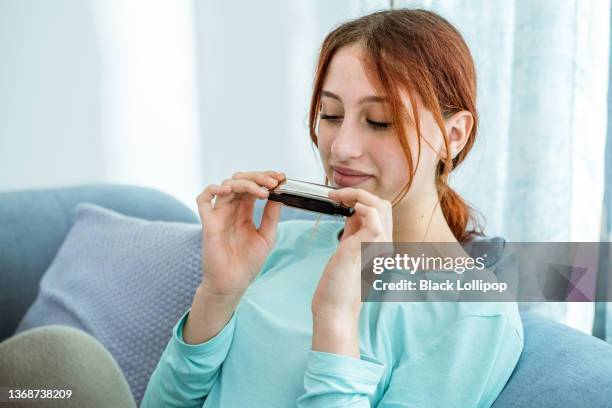 teenager-mädchen spielt mundharmonika, mundakkordeon in einem wohnzimmer. - harmonica stock-fotos und bilder