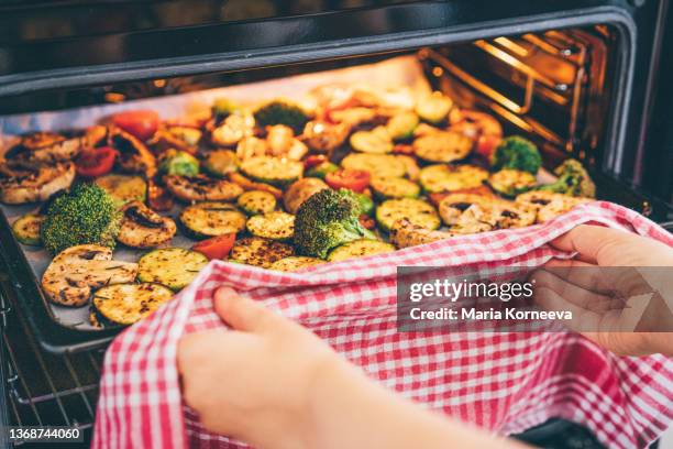 woman putting a tray of vegetables in the oven. - geröstet stock-fotos und bilder
