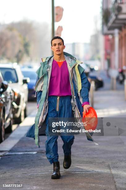 Guest wears a neon purple with orange V-neck pullover, a green / gray / pale yellow / blue long oversized K-way coat, matching blue K-way sport...