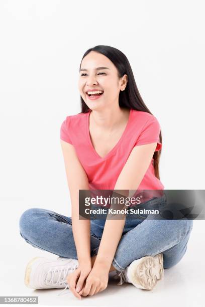 beautiful young woman with black hair sitting on the ground against white background - gambe incrociate foto e immagini stock
