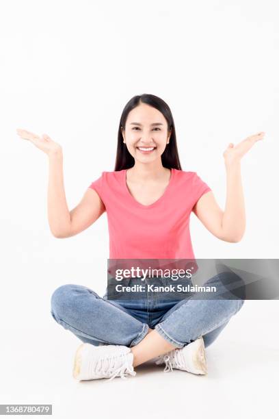 portrait of smiling woman gesturing while sitting on ground against yellow background - woman plain background stock pictures, royalty-free photos & images