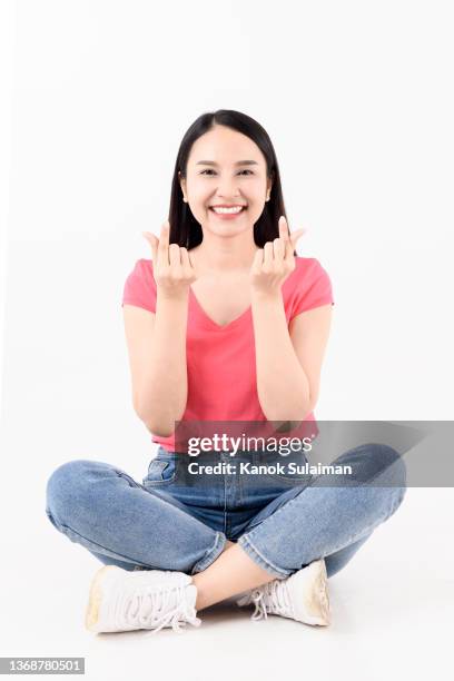 portrait of smiling young woman sitting on ground and snapping fingers against white background - clicking fingers stock pictures, royalty-free photos & images