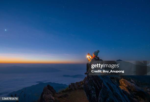 tourist woman holding a lantern while sitting on the rock on top of doi pha tang mountain a high cliff over the thai-laotian border located in wiang kaen district of chiang rai province of thailand. beautiful view before the sunrise. - women's tour stock-fotos und bilder