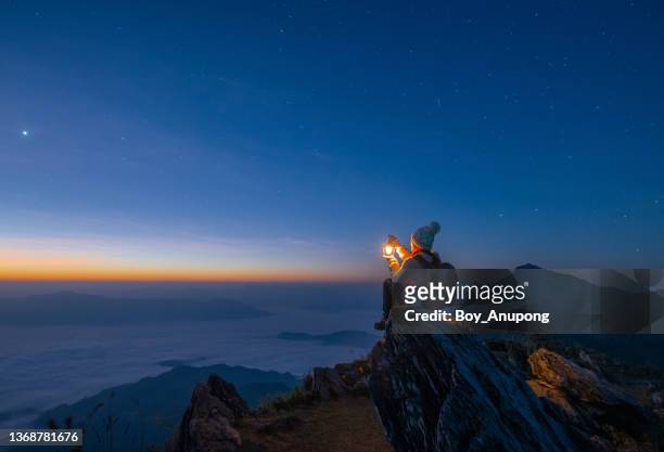 tourist woman holding a lantern while sitting on the rock on top of doi pha tang mountain a high cliff over the thai-laotian border located in wiang kaen district of chiang rai province of thailand. beautiful view before the sunrise. - jack o lantern fotografías e imágenes de stock