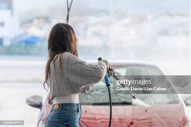 rear view of an african american woman about 40 years old washing his car in a washing car station. - high pressure cleaning - fotografias e filmes do acervo