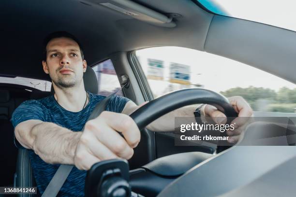 young excited driver holding a steering wheel with his hands looks forward curiously while driving a car at a high speed on the freeway. a man wearing a seat safety belt inside a vehicle - road safety stock pictures, royalty-free photos & images