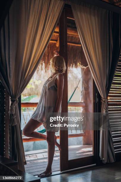 young woman leaning on a  wooden balcony door of a beautiful bamboo house. - thatched roof huts stock pictures, royalty-free photos & images