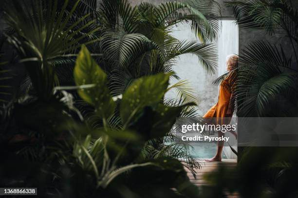 frau lehnt sich an eine graue betonsteinmauer, umgeben von grünen tropischen palmblättern, am pool. - palmenblätter stock-fotos und bilder
