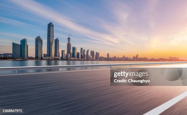 auto advertising backplate. empty road in front of magnificent sunrise glow over qingdao city skyline - voie urbaine photos et images de collection