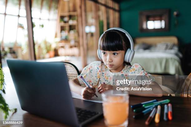 concentrated asian girl with headphones studying from home. she is attending online school classes with laptop and writing notes at home. e-learning, homeschooling concept - china exam imagens e fotografias de stock