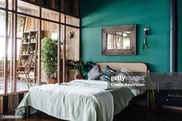 ein stilvolles loft-schlafzimmer mit braunen rattanmöbeln und holzelementen mit dunkelgrüner wand. dekoriert mit pflanzen - boho stock-fotos und bilder