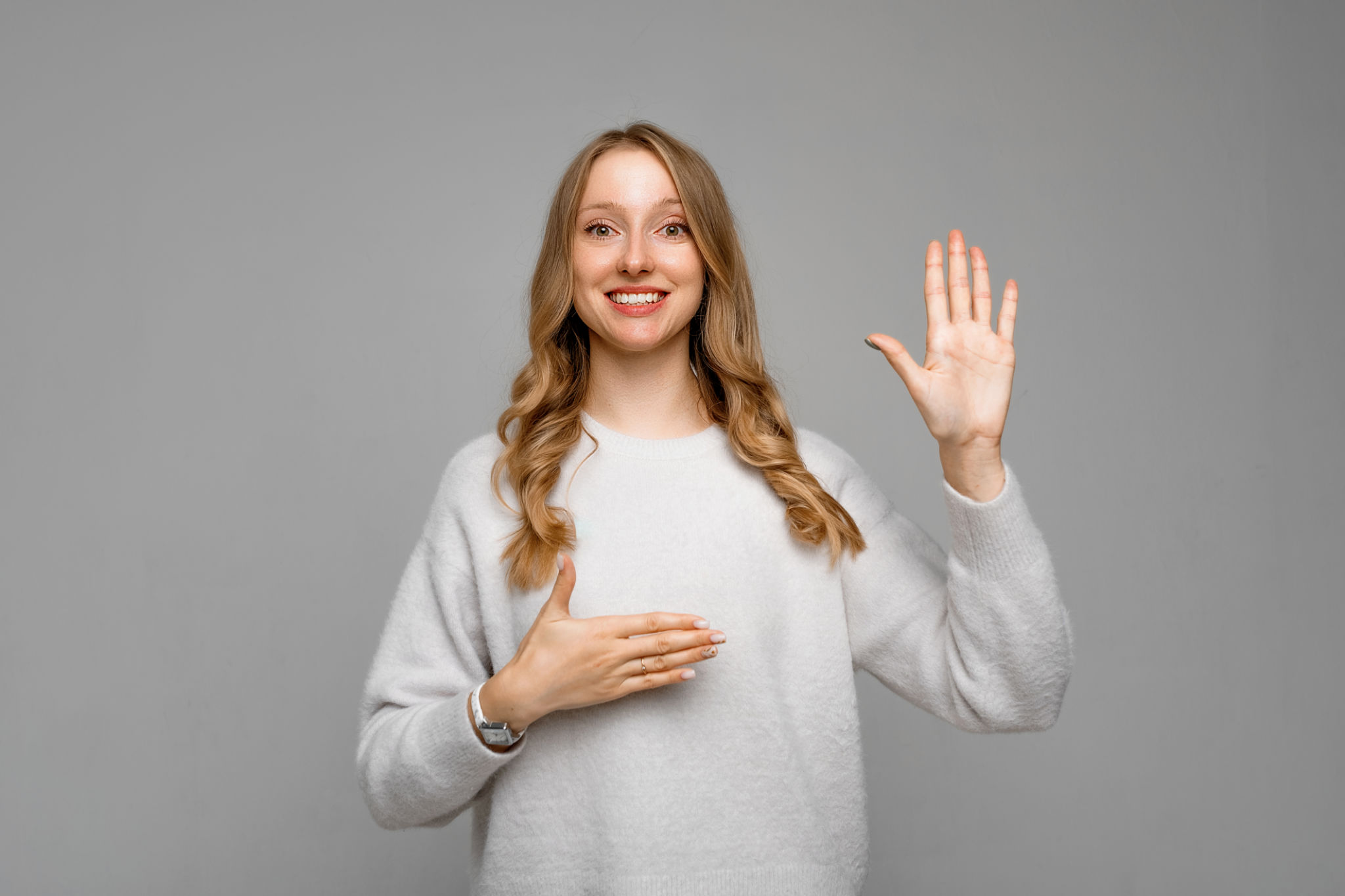 Smiling responsible and honest woman, raising hand and holding palm on heart, making promise, looking happy, wears white sweater, stands over gray background Smiling responsible and honest woman, raising hand and holding palm on heart, making promise, looking happy, wears white sweater, stands over gray background