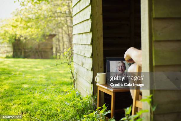 man video chatting with friends on laptop from garden shed - northern europe stock pictures, royalty-free photos & images