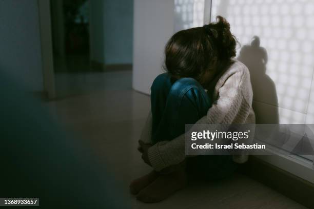 unrecognizable young girl sitting on the floor of her room with her head resting on her knees. - kids invasion stock pictures, royalty-free photos & images