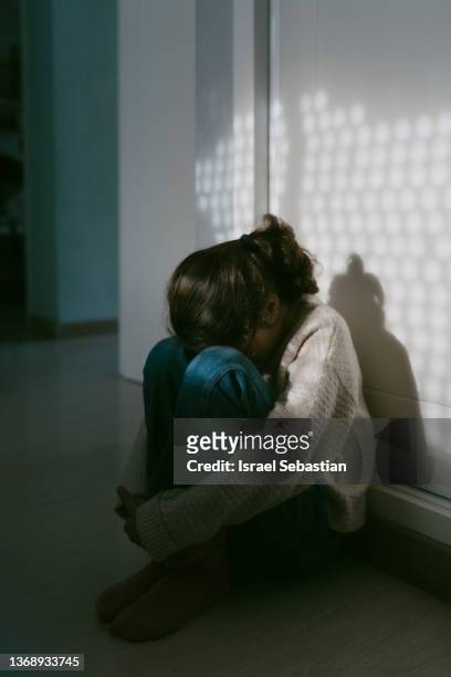 portrait of an unrecognizable young girl sitting on the floor of her room with her head resting on her knees. - cyberbullying stock-fotos und bilder