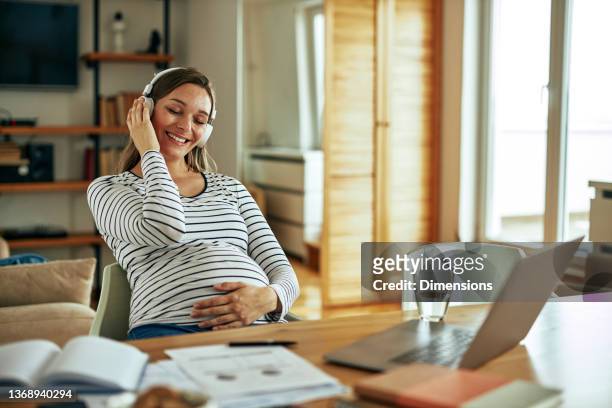 frau, die die schwangerschaft zu hause genießt und musik hört - budget hearing stock-fotos und bilder