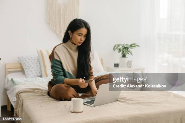 woman holding credit card while doing shopping online on modern laptop at home - kazakhstan stock pictures, royalty-free photos & images
