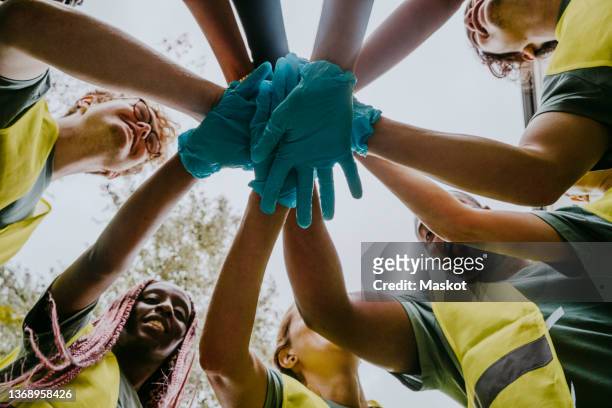 volunteers wearing gloves bringing hands together - ngo imagens e fotografias de stock