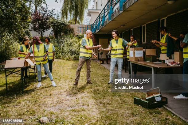 male and female volunteers helping each other while working in garden - tolerancia fotografías e imágenes de stock
