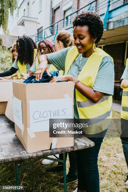 smiling female volunteer arranging clothes in donation box at garden - community garden volunteer stock pictures, royalty-free photos & images