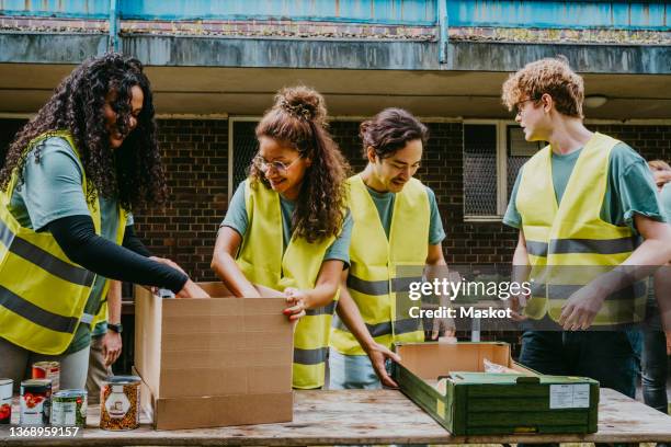 smiling male and female friends working at table in non-profit organization - volunteerism stockfoto's en -beelden