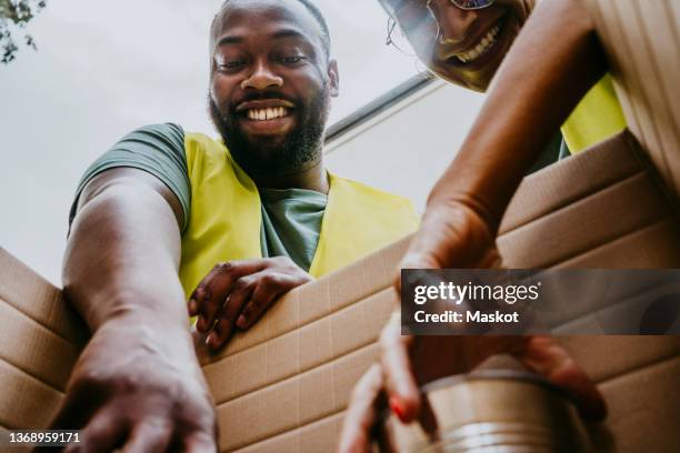 happy female and male heroes arranging canned foods in box - banco alimentare foto e immagini stock