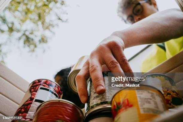 young man holding canned food in box - food pantry stockfoto's en -beelden