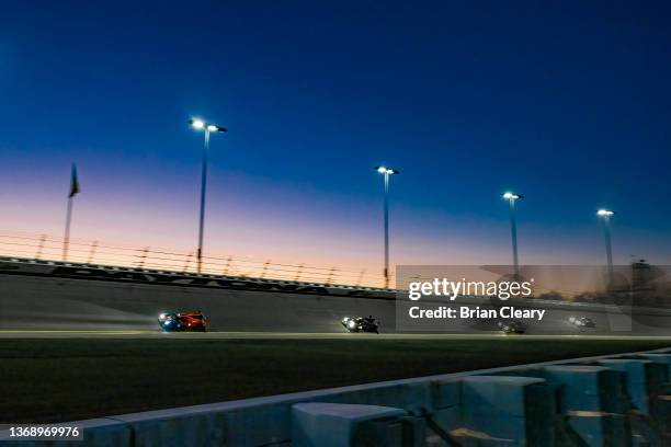 Pack of cars races through the banking at sunrise during the Rolex 24 during the IMSA WeatherTech Series race at Daytona International Speedway on...