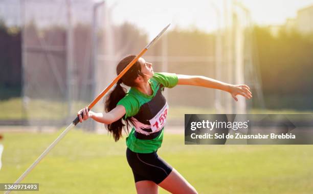 brunette girl with ponytail throwing the javelin on a beautiful sunny day - jabalina fotografías e imágenes de stock