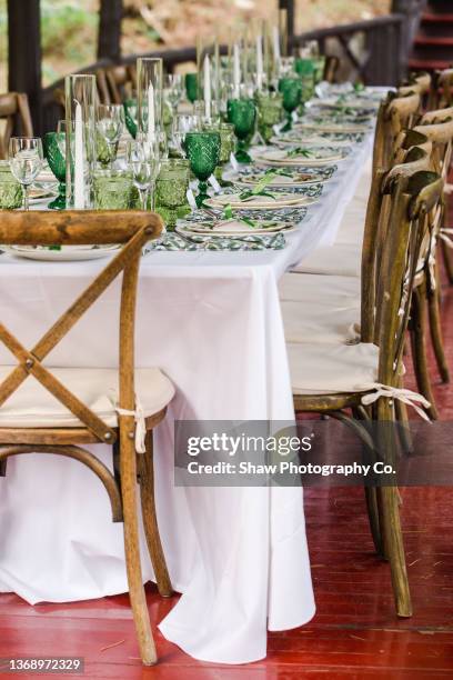 detailed shot of a long table set up for dinner at a green and nature inspired wedding. it is full of candles, plates, decorations, silverware, and table settings including green water glasses and green-rimmed plates - big wedding reception stock pictures, royalty-free photos & images