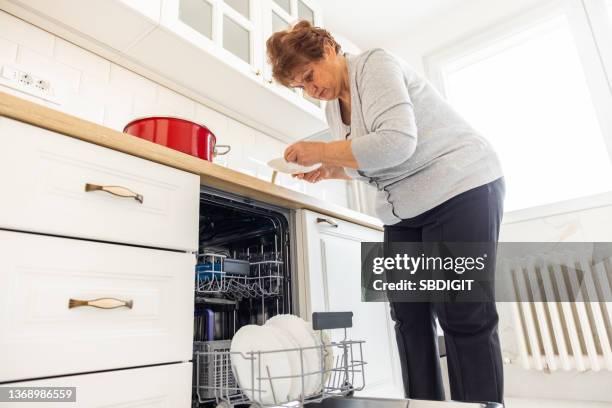 senior woman loads dishwasher - vaatwastablet stockfoto's en -beelden