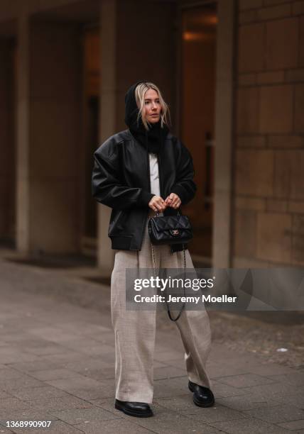 Kathrin Bommann wearing Chanel black leather bag, Mentlova black oversized leather jacket, black balaklava, COS beige linen pants and black boots on...