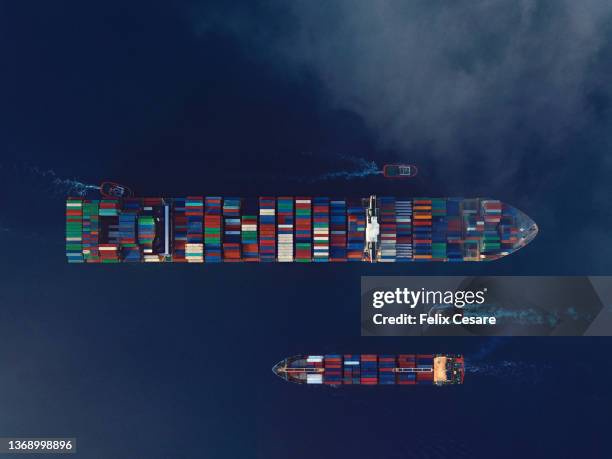 aerial view of two cargo ships being guided by tugboats. shipping container trading business. - tariff stock pictures, royalty-free photos & images